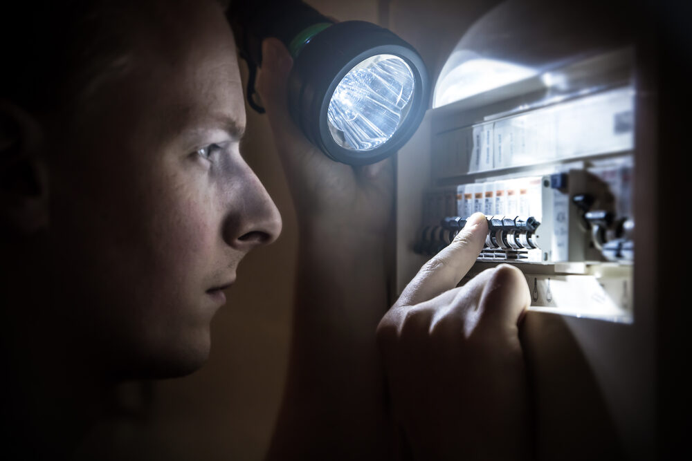 Electrician inspecting a panel with a flashlight